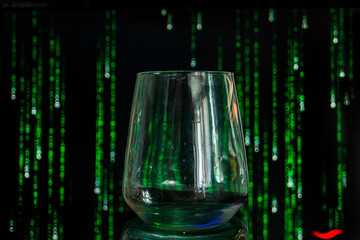 A glass of water stands against the background of a monitor with falling numbers and letters	
