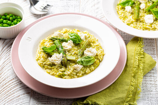 Risotto with green pea and asparagus with robiola cheese on a pink plate. Homemade spring rice food on a white table.