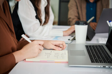 Businesswoman sitting at office table with colleagues, drinking coffee and taking notes in planner