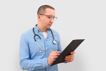 Male doctor making notes on a clipboard on a gray studio background.