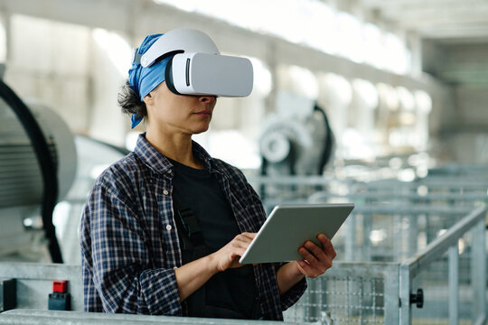 Female engineer connecting tablet pc with VR glasses and using them in her work in factory