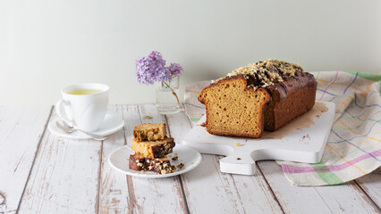 Pieces of delicious, sweet cupcake on white saucer, cup of tea, sprig of lilac on wooden background with linen napkin. Homemade cakes, sweet bread. Selective focus. Copy space