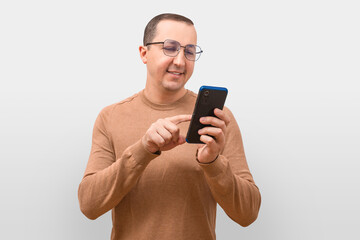 A young man in a sweater uses a phone on a gray background.
