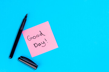 Pink note with inscription Good day and marker on blue background, flat lay.