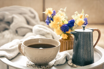 Home composition with a cup of tea and flowers on a blurred background.