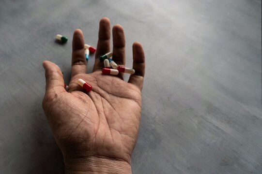 Closeup image of hand and pills on concrete floor with copy space. Overdose, drug addict and suicide concept