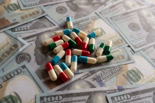 Selective focus image of colorful pills on top of money. Medical expenses and pharmaceutical industry concept