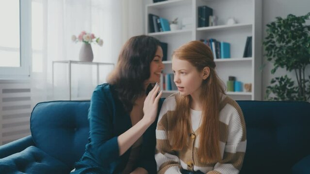 Middle-aged mother whispering a secret to her teenage daughter, family bonding