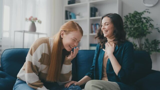 Happy middle-aged woman laughing with her teen daughter at home, friends