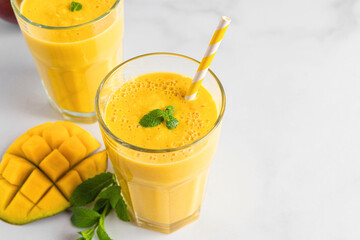 Fresh yellow mango smoothie in glasses with straw, fresh fruits and mint. Summer tropical drink