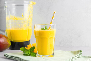 Glass of yellow mango smoothie with fresh juicy fruits and blender for making healthy summer drink