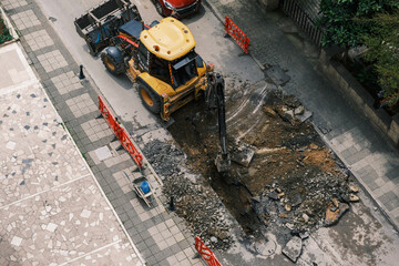 An excavator repairs sewer storm hatches ata street on a summer day. Selective Focus Machine. Top...