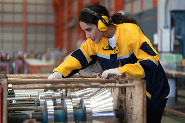 Female industrial engineer in white helmet, safety jacket and headphone work in heavy metal...