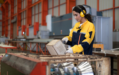 Female industrial engineer in white helmet, safety jacket and headphone work in heavy metal...