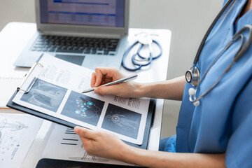 Close up of young female doctor summarizing patient chart with digital pad in her white office