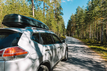 Silver car with roof trunk traveling in green summer forest in Finland.