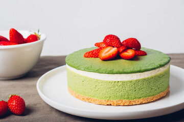 Layered ice cream matcha cheesecake decorated with fresh strawberry. Gluten free no bake dessert, close up. Healthy sweet food.