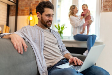 Father working on laptop, mother and daughter on background playing.