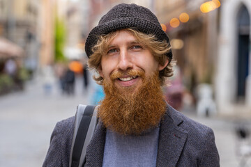 Close-up portrait of happy young adult man face smiling friendly, glad expression looking at camera dreaming, resting, relaxation feel satisfied good news outdoors. Bearded guy in urban city street