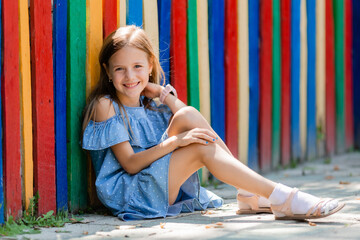 portrait of a happy little girl in summer sitting on the background of a colored fence in a...