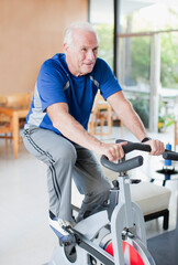 Fototapeta na wymiar Older man riding exercise bike at home