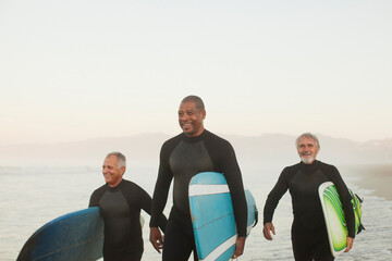 Older surfers carrying boards on beach