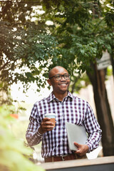 Fototapeta premium Man carrying coffee and laptop on city street