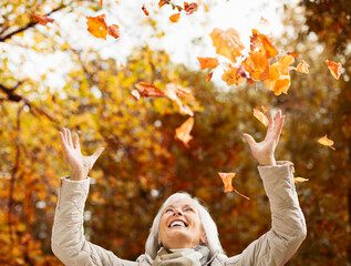 Older woman playing in autumn leaves