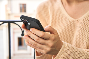 Redhead woman types on phone at balcony, immersed in urban view behind her.