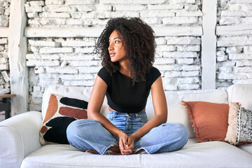 Afro-haired woman relaxes on sofa, basking in soft morning light at home.