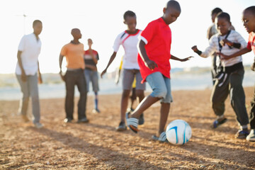 Boys playing soccer together in dirt field