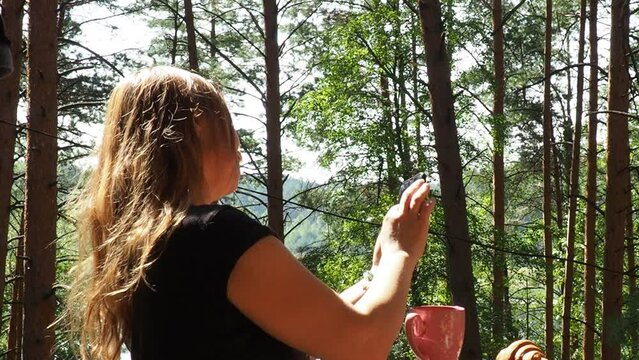 Happy woman relaxing and looking forest and lake at countryside home or homestay in the morning. drinks tea or coffee. taking photos and selfies. Vacation, blogger, SoloTravel, journey, trip
