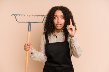 Young african american gardener woman holding a rake isolated having an idea, inspiration concept.