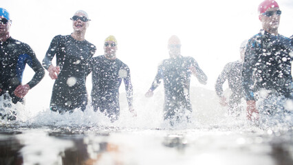 Triathletes in wetsuits running in waves - obrazy, fototapety, plakaty