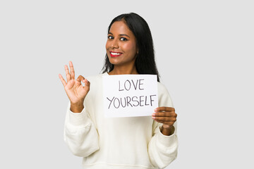 Young Indian woman holding a love yourself placard isolated on white background - Powered by Adobe
