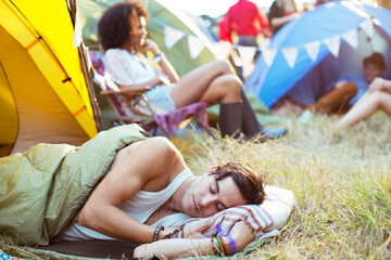 Man sleeping in sleeping bag outside tent at music festival