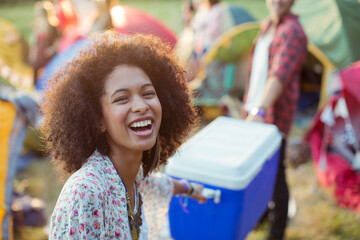Portrait laughing woman helping man carry cooler outside tents at music festival