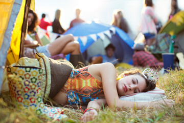 Woman tiara sleeping in sleeping bag outside tents at music festival