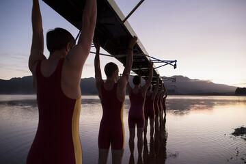 Rowing team carrying boat overhead into lake - obrazy, fototapety, plakaty