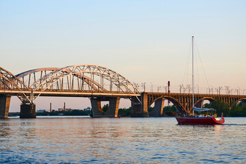 A large bridge on an evening calm river and a pleasure yacht