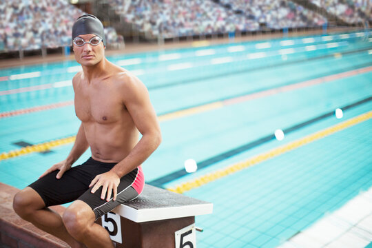 Swimmer sitting on starting block at poolside