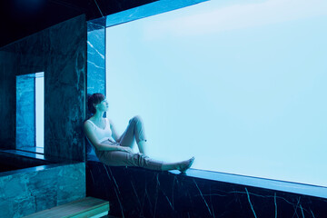 Woman sitting on window ledge looking at underwater view of swimming pool