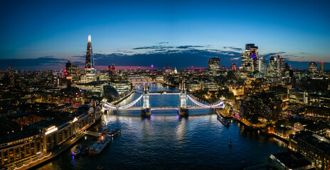 Panoramic aerial view of the famous Tower Bridge and river Thames with the illuminated City skyscrapers during night time, England