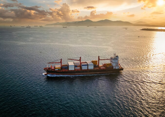 Aerial view of a medium sized container cargo ship sailing over calm sea during sunset time