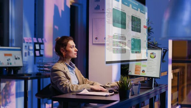 Employee checking analytics hologram in office at night, looking at holographic images of company archive reports. Executive manager using online information, presentation support.