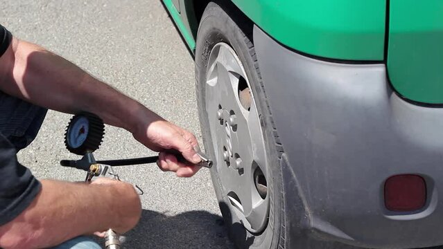 Driver Inflating Car Tire. Hand Holding Hose with Air Pressure Gauge and Filling Up Car's Tire with Air.  Checking Tire Pressure.