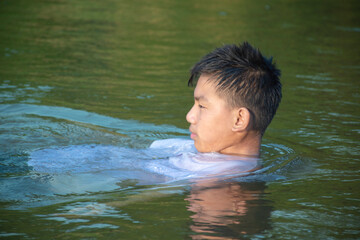 Asian boy in white t-shirt is spending his freetimes by diving, swimming, throwing rocks and catching fish in the river happily, hobby and happiness of children concept, in motion.