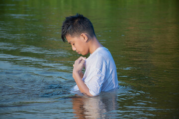 Asian boy in white t-shirt is spending his freetimes by diving, swimming, throwing rocks and catching fish in the river happily, hobby and happiness of children concept, in motion.