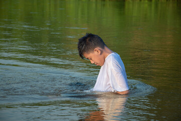 Asian boy in white t-shirt is spending his freetimes by diving, swimming, throwing rocks and doing masturbation in the river happily, hobby and happiness of children concept, in motion.
