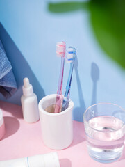 Toothbrushes in cup, toothpaste, cotton pads and bath towels on blue background